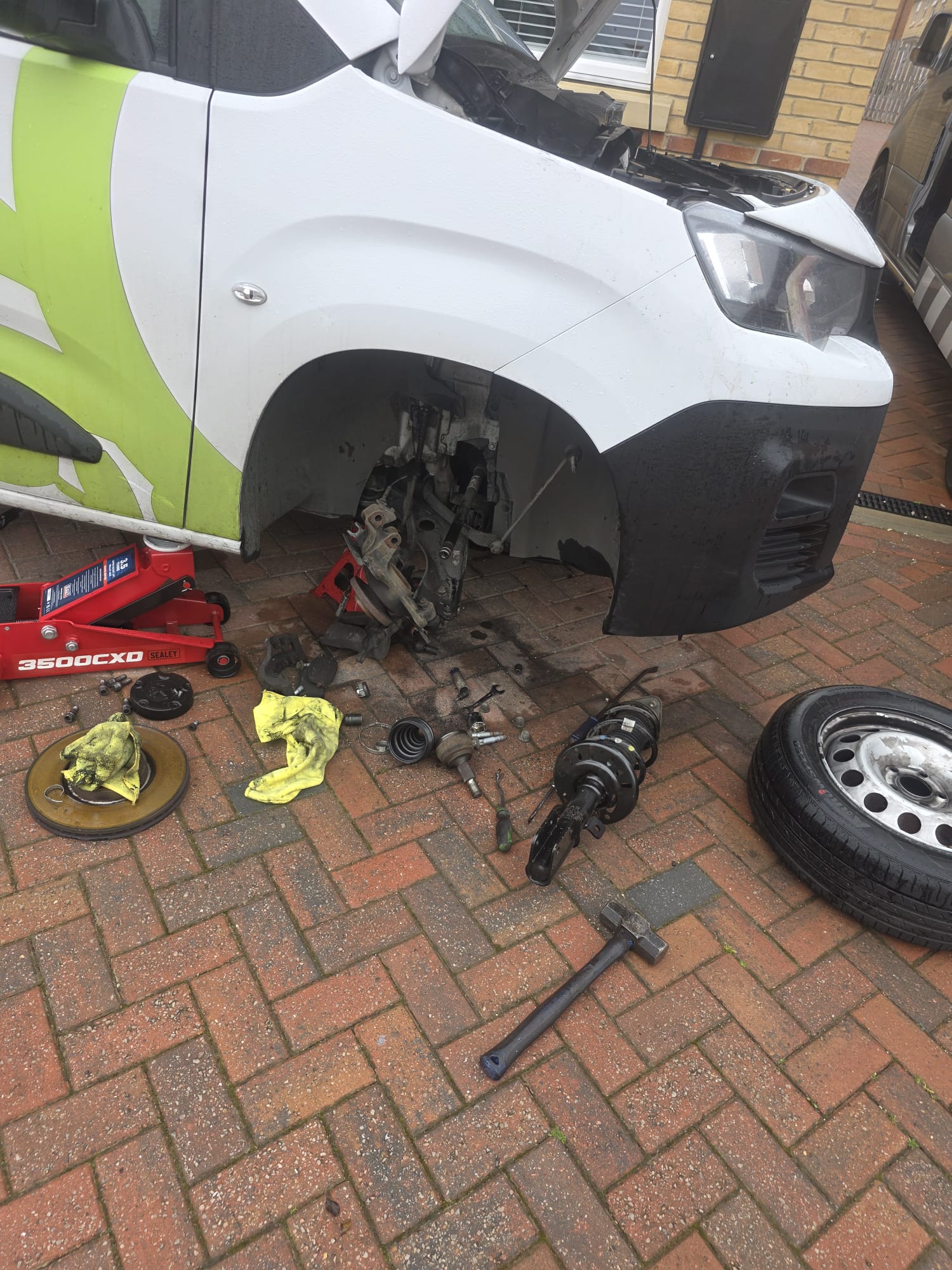 A customer van with a wheel off and suspension parts laid out on the driveway