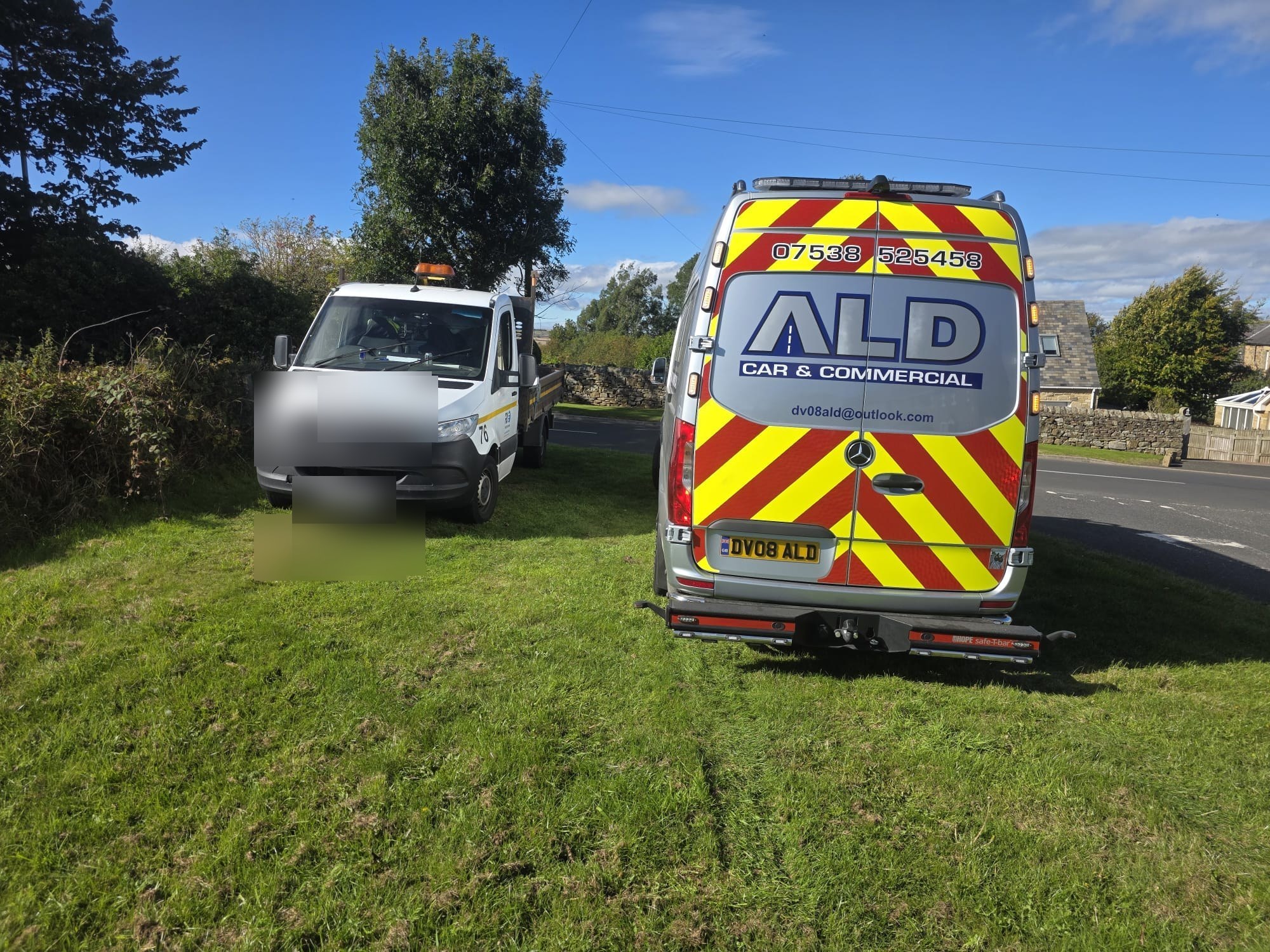 An ALD van parked behind a white recovery truck on a country road