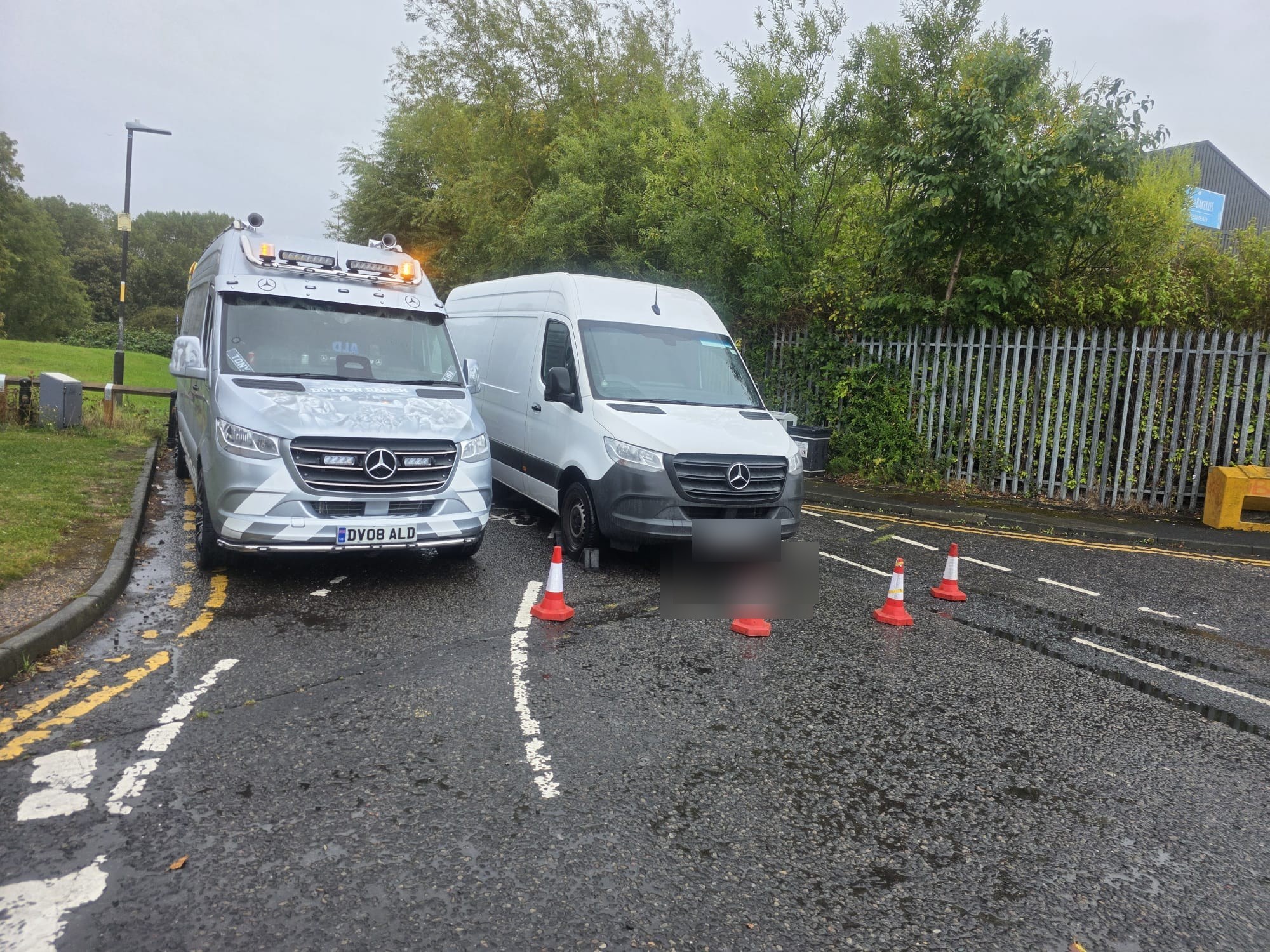 An ALD van parked beside a customer van behind traffic cones on a wet roadside